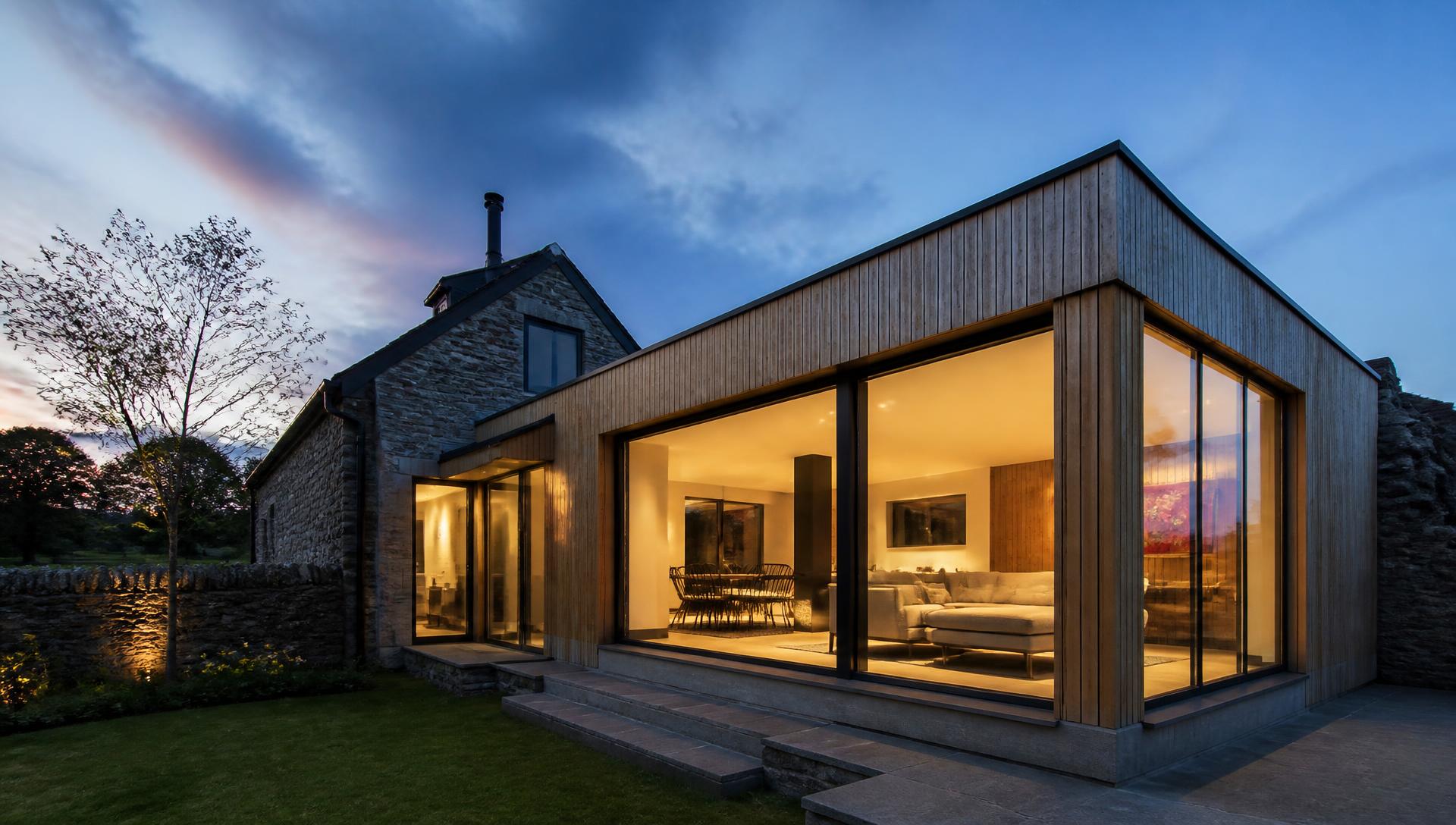 Oak-clad modern home extension lit from within at dusk